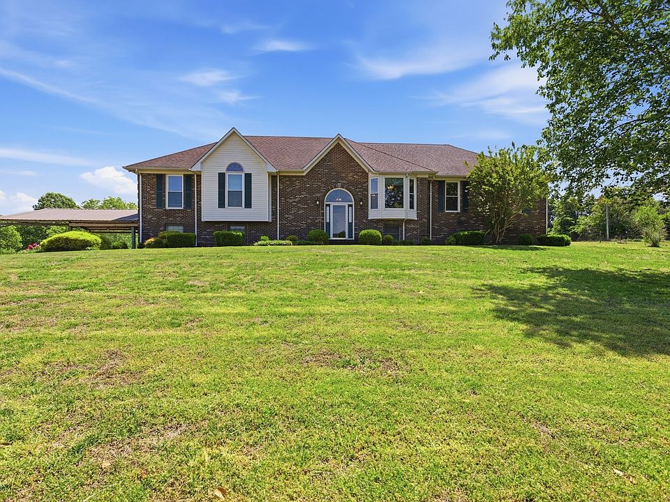 Front elevation of 1474 Hardison Rd, the multi-level brick contemporary country home set back on a wide open lawn under a clear Tennessee sky