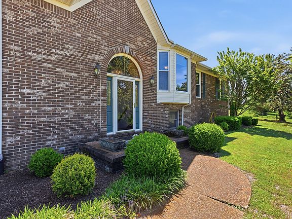 Detail of the arched front entry of 1474 Hardison Rd, blue shutters flanking a tall transom window, brick steps and clipped boxwoods leading to the door